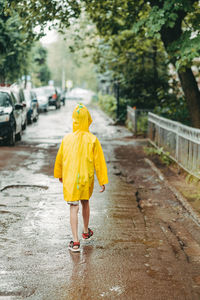  boy in a yellow raincoat comes out in the rain. child alone walks in the rain. 