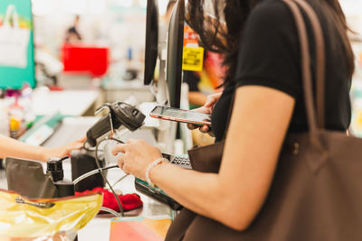 Woman customer scanning qr code payment via mobile phone at cashier counter in store.