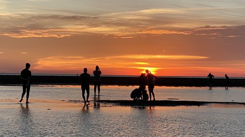 Silhouette people on beach against sky during sunset