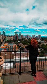 Rear view of woman standing against sky in city