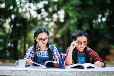 Friends reading book while sitting against trees