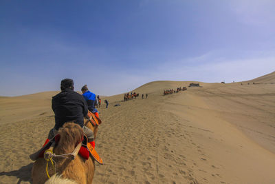 Rear view of people riding on camel train
