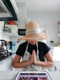 Mature woman wearing hat gesturing while standing in kitchen