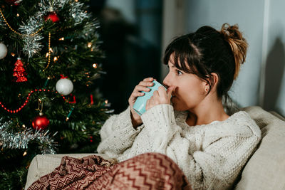 Portrait of young woman holding christmas tree at home