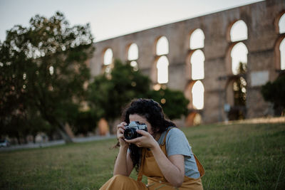 Woman photographing through camera against built structure