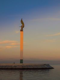 Statue on wooden post by sea against sky during sunset