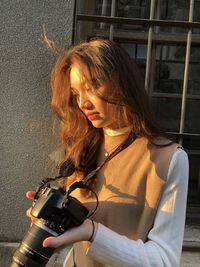Young woman holding camera while standing outdoors