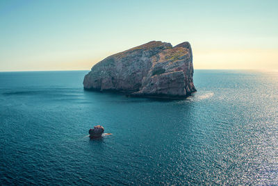 Rock formation in sea against sky during sunset