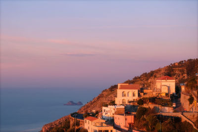 Buildings by sea against sky during sunset