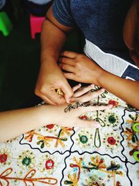 High angle view of female drawing henna tattoo on woman hand