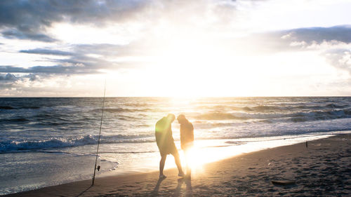 Rear view of silhouette man standing at beach during sunset