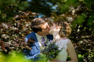 Affectionate wedding couple kissing amidst plants at park