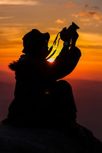 Silhouette woman photographing from camera against sky during sunset