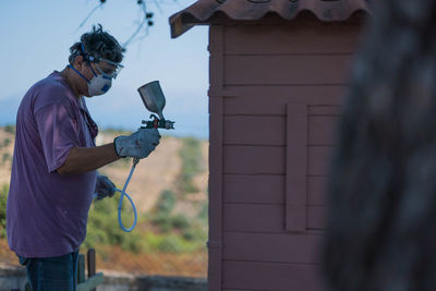 Man spraying paint over log cabin