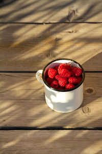Fresh organic raspberries in white cup on wooden background