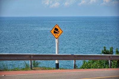 Road sign by sea against sky