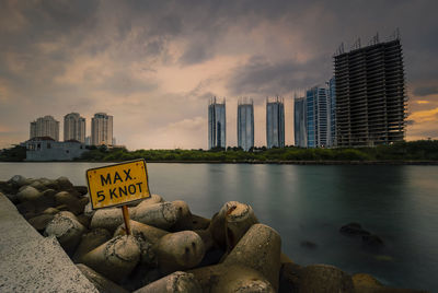 Rocks by sea against buildings in city during sunset