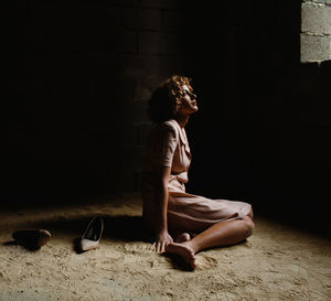 Side view of woman looking away while sitting on floor in darkroom