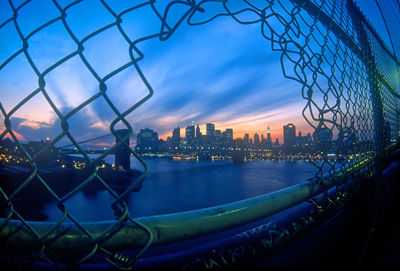 Manhattan skyline seen from broken chainlink fence during sunset