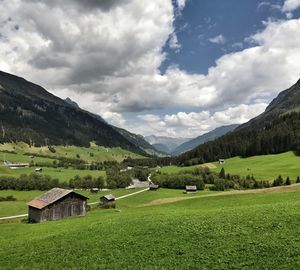 Houses on land by mountains against cloudy sky