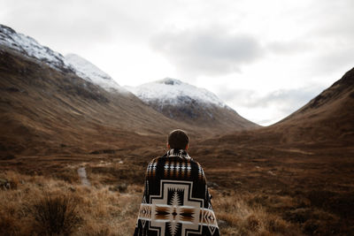 Back view of unrecognizable male explorer standing enjoying scenery of mountains in fall in scottish highlands