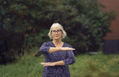 Portrait of woman gesturing while standing on footpath against buildings