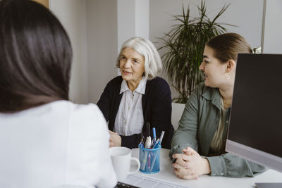 Senior woman by daughter discussing with doctor during visit in clinic