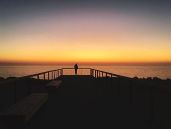 Silhouette man standing on beach against clear sky during sunset
