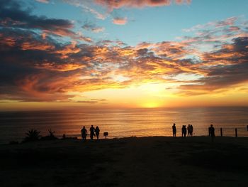 Silhouette people at beach against sky during sunset