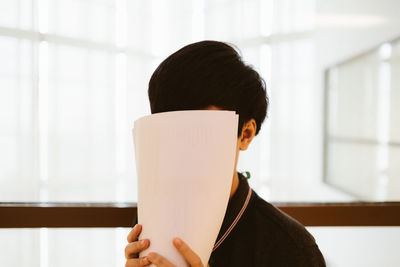 Close-up of young woman hiding face with papers at office