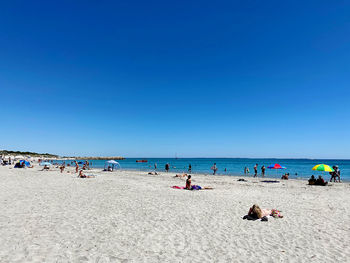 Group of people on beach against clear blue sky