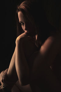Young woman looking away while sitting against black background