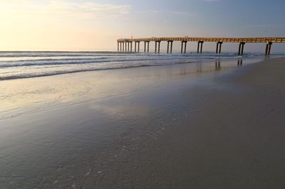 Pier on beach against sky during sunset