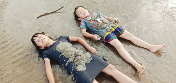 High angle view of siblings lying on beach