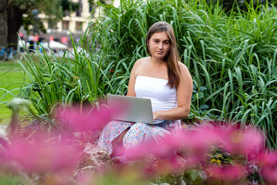 Portrait of young woman using laptop sitting against plants