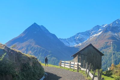 Rear view of woman walking towards mountains against clear blue sky