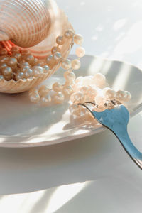 Close-up of pearls with seashell and fork in plate on table
