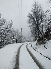 Snow covered road amidst bare trees against sky