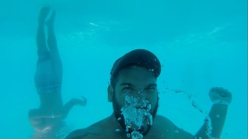 Upside down image of shirtless male friends swimming in turquoise sea