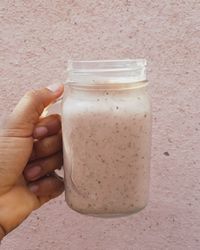 Cropped hand holding smoothie in jar against wall