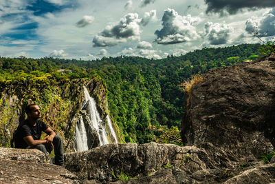 Man sitting on rock against sky