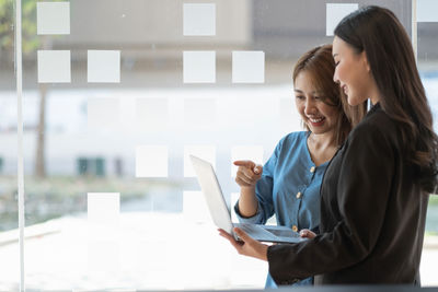 Side view of woman using mobile phone while standing in office