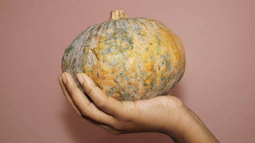 Close-up of man holding pumpkin against orange background