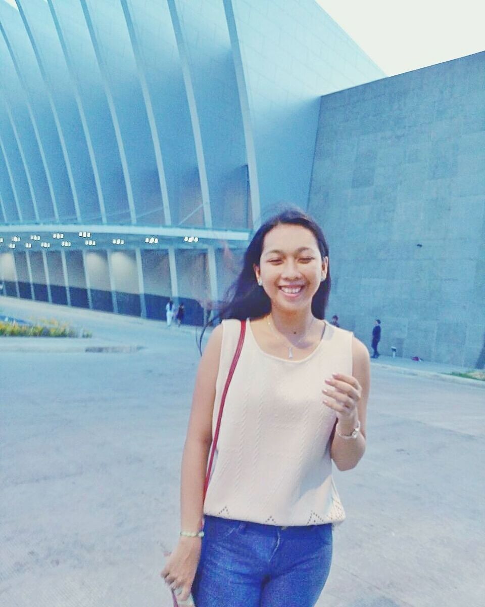 PORTRAIT OF SMILING YOUNG WOMAN USING PHONE WHILE STANDING ON MOBILE