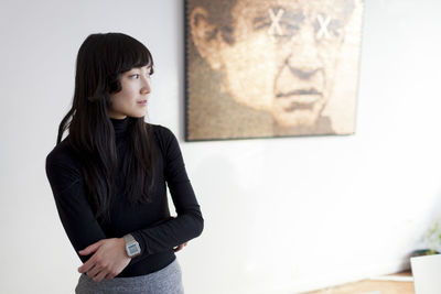 Young woman looking away while standing against wall