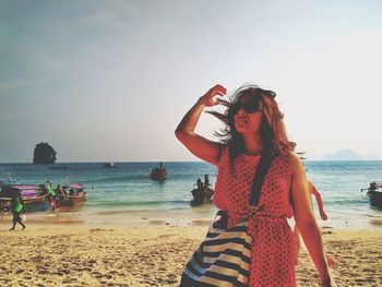 Woman looking up while standing at beach against sky