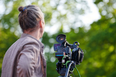 Rear view of man photographing against trees