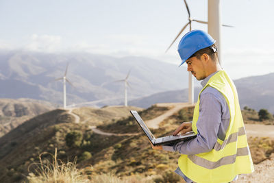 Engineer using laptop in front of wind turbines on sunny day