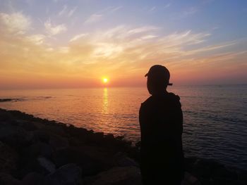 Rear view of silhouette man standing at beach during sunset