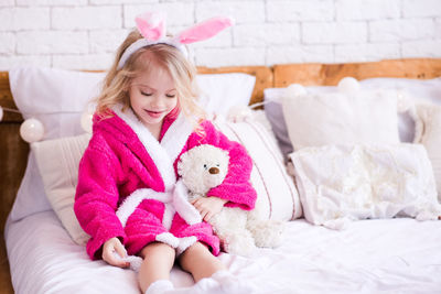 Girl in bathrobe playing with teddy bear on bed
